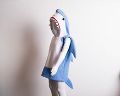 a white and blue stuffed shark with its mouth open, standing next to a wall