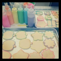 two trays filled with decorated cookies on top of a table next to bottles and markers