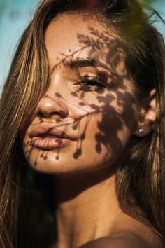 a woman's face is shown with the shadow of a tree on her cheek