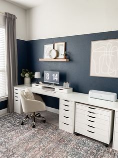 a white desk sitting in front of a window next to a wall with pictures on it