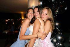 three girls hugging each other in front of balloons