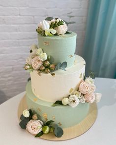 a three tiered cake with flowers and greenery on the top is sitting on a table