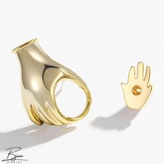 two gold rings with hands on them sitting next to each other, one is shaped like a hand