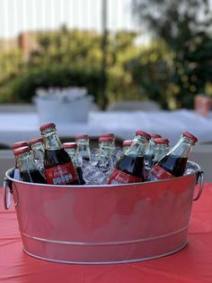 a metal bucket filled with bottles of beer on top of a red cloth covered table