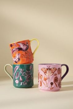 three different colored mugs with designs on them