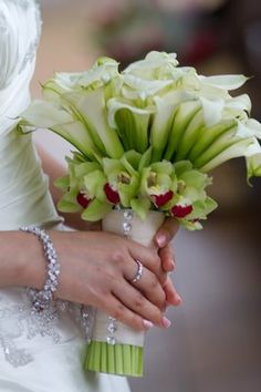 a woman in a wedding dress holding a bouquet of white and green flowers with jewels on her wrist