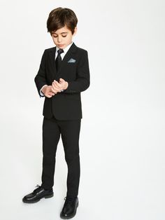 a young boy in a suit and tie standing with his hands folded over his chest