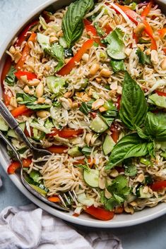 a white bowl filled with noodles and veggies on top of a blue table