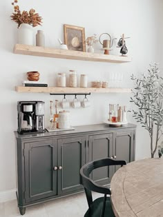 there is a coffee maker on the shelf above the counter in this kitchen with gray cabinets and black chairs