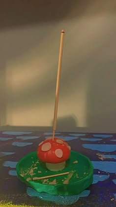 a red mushroom on top of a green plate with a wooden stick sticking out of it