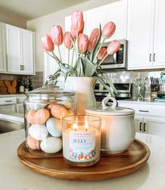 a candle and some flowers in a glass jar on a wooden platter with eggs