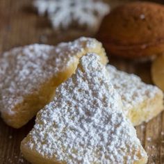 three pieces of powdered sugar sit on a wooden table next to some nuts and other food