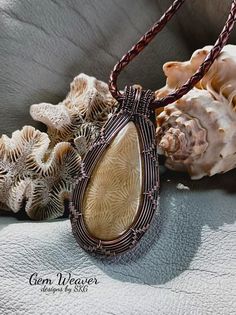 a brown wire wrapped pendant sitting on top of a white surface next to sea shells