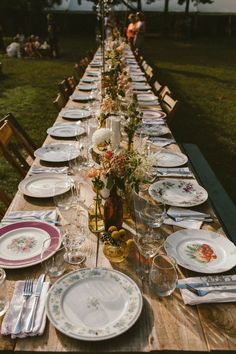 a long table set with plates and silverware for an outdoor dinner in the grass