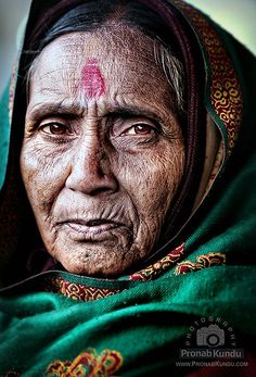 an old woman wearing a green shawl with a red cross on her forehead and eyes