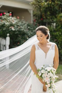 a woman in a wedding dress is holding a bouquet and veil over her head while she smiles at the camera