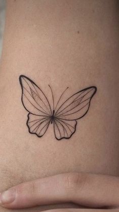 a small butterfly tattoo on the back of a woman's left arm, which is black and white