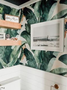 a bathroom decorated with tropical wallpaper and pictures on the shelf above the toilet area