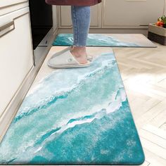 a woman standing on top of a blue rug next to a kitchen sink and oven