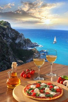 two glasses of wine and a pizza on a table with the ocean in the background