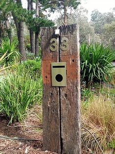 a wooden post with a house number on it in the middle of some grass and trees