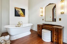 a white bath tub sitting next to a wooden dresser in a bathroom on top of a hard wood floor