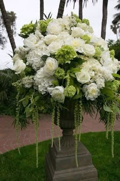 a large vase filled with white flowers on top of a green planter in front of palm trees