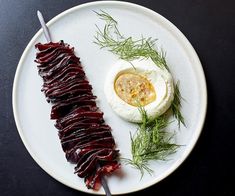 a white plate topped with meat and an egg on top of a black table next to a fork