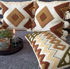 two decorative pillows with tassels and a candle on a tray next to them