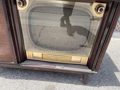 an old tv sitting on top of a sidewalk next to a metal object with a shadow cast on it