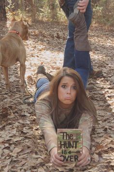 a woman laying on the ground with a book in front of her and a dog standing behind her