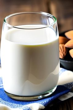 a glass filled with milk sitting on top of a blue and white cloth next to nuts