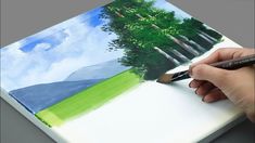 a person is holding a paintbrush and drawing on a piece of paper with trees in the background