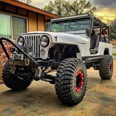 a white jeep parked in front of a building with red rims on it's tires