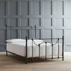 an iron bed frame with white sheets and pillows on it in front of a gray wall