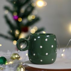 a green polka dot coffee cup sitting on top of a plate next to a christmas tree