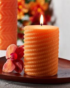 an orange candle sitting on top of a wooden plate next to a red and yellow flower