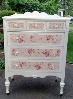 a white dresser with pink flowers painted on the top and bottom drawers, sitting in front of some trees