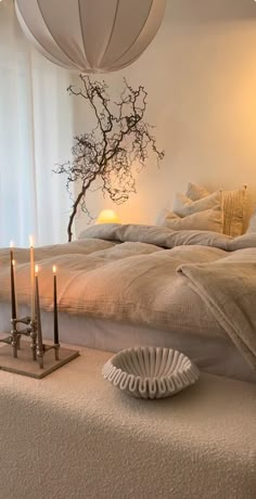 a bed with two candles on it next to a vase and some branches in the background