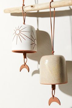 two ceramic bells hanging from hooks on a white wall next to a wooden stick with a sun and moon design