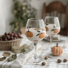 two wine glasses with pumpkins painted on them sitting on a table next to nuts