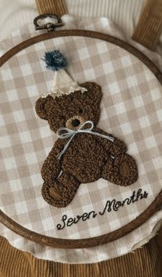 a brown teddy bear sitting on top of a white checkered table cloth next to a wooden hoop