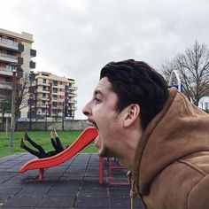 a man with his mouth wide open is sitting on a red slide in the park