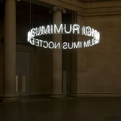 an illuminated sign in the middle of a room with columns and pillars on either side