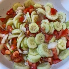 a white bowl filled with sliced cucumbers, tomatoes and other veggies