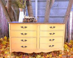 an old dresser is painted yellow with black trim and gold leafy leaves on the ground