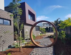 a circular sculpture in the middle of a gravel garden area next to a brick building