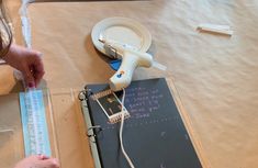 a woman is cutting paper with scissors and tape on the table next to a binder