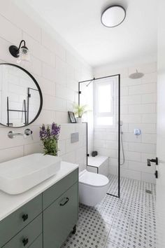 a white bathroom with black and white tile flooring, round mirror above the sink