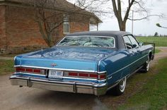 an old blue car parked in front of a brick building on a dirt road next to a tree